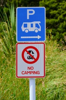 Ein Schild zeigt einen Parkplatz für Wohnmobile und ein Verbotsschild für Camping vor grüner