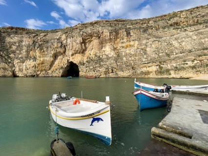 Moored excursion boat without tourists in inland sea of Gozo, in the background tunnel from passage