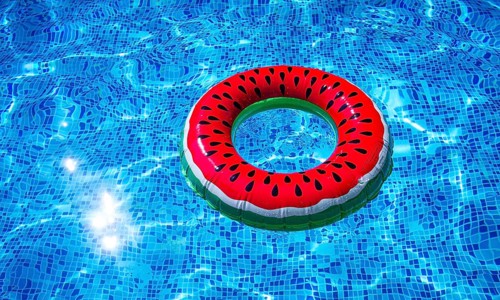 A bright ring-a float, with a watermelon, in the clear blue water of the pool, under the sunlight