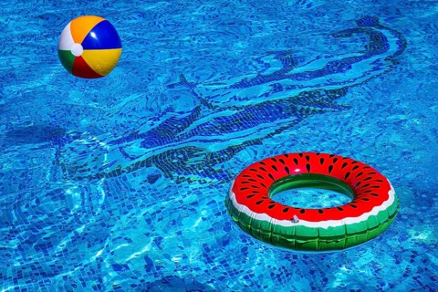 Colorful beach ball and watermelon circle, floating in the pool water, on a sunny summer day, no