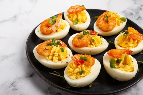 Boiled eggs stuffed with yolk and seasoned with mayonnaise, stuffed eggs with shrimp, on a black