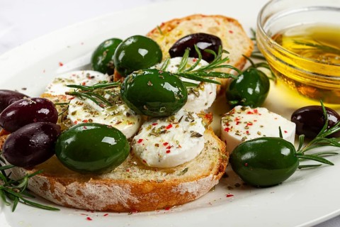 A plate with a snack, ciabatta bread with cheese and olives, olive oil, spices and herbs, top view,
