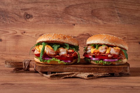 Two shrimp burgers and buns with sesame seeds, bacon, lettuce, tomatoes and onions, on a wooden
