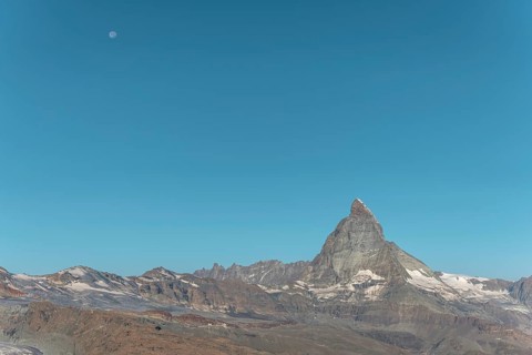 The iconic Matterhorn stands high above a clear evening sky illuminated by a bright moon. This