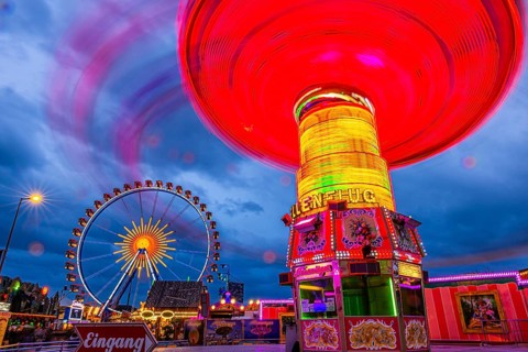 Illuminated chain carousel in motion, behind the Ferris wheel at standstill, Festwiese,