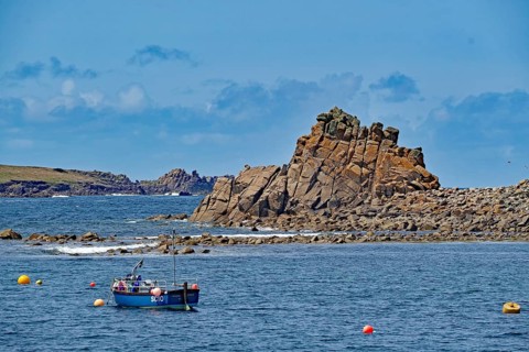 Rocky coastal landscape with a small boat and colourful buoys under a blue sky, Isles of Scilly,