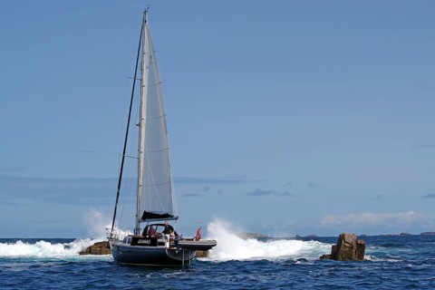 A sailing boat navigates through rocky sea with blue sky in the background, Isles of Scilly,