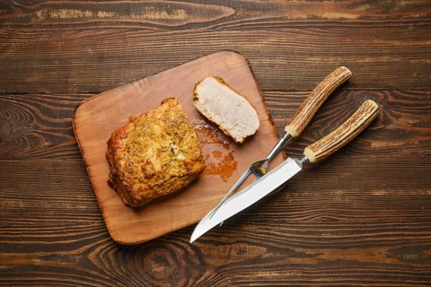 A deliciously roasted piece of pork meat on a wooden cutting board served with carving knife and