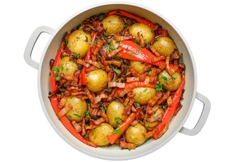 Golden baby potatoes are roasted with vibrant red peppers and crispy bacon isolated on white