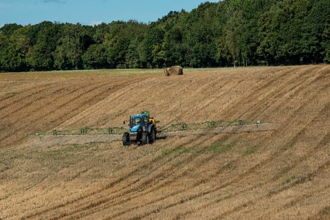 Tractor spreading fertilizer on harvested stubble field in Ystad municipality, Skåne county,