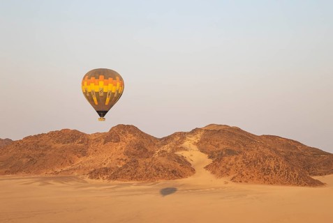 The hot-air balloon above an arid plain and isolated mountain ridges at the edge of the Namib