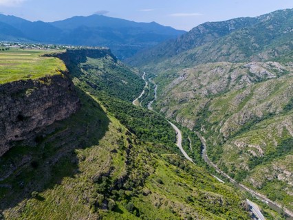 View of a picturesque valley with a river, surrounded by high mountains and lush vegetation under a