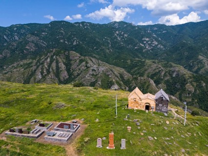 Old church and cemetery on a green mountain under a blue sky with clouds, aerial view, landscape
