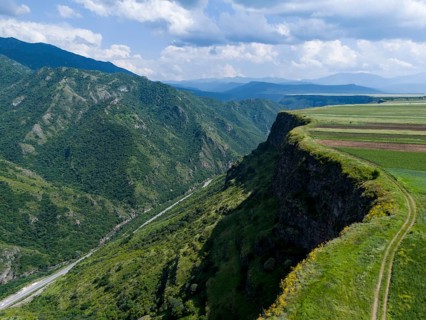 Steep slope with a view of the wide valley and patterned fields under a blue sky, aerial view,