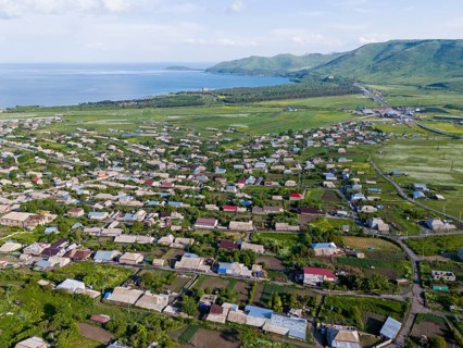 Vast landscape with houses and green fields by the sea and mountains in the distance, aerial view,