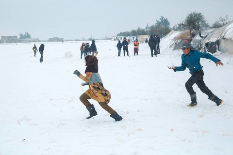 Displaced Syrian children playing in the snow near their tents inside a refugee camp during winter.