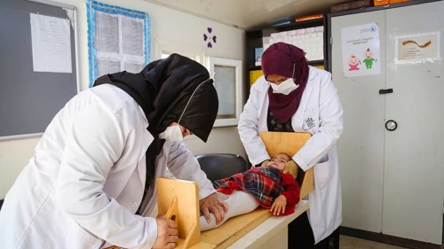 A doctor examining a refugee child for malnutrition in the camp using weight and height measurement