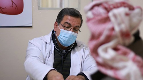 A Syrian doctor wearing a protective mask consults with a displaced patient inside a medical clinic