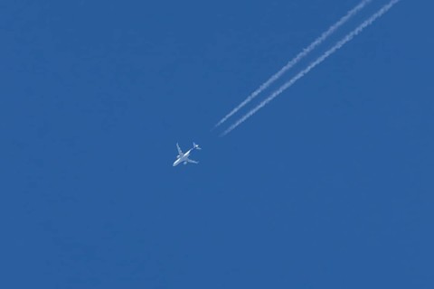 Jet passenger aircraft with a vapour trail or contrail flying in a blue sky, England, United