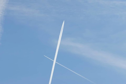 Two jet passenger aircraft with vapour trails or contrails flying in a blue sky crossing making a