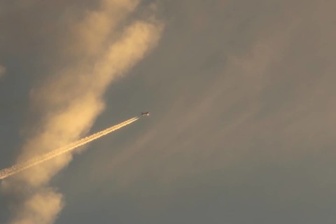 Jet passenger aircraft with a vapour trail or contrail flying in a sky with clouds, England, United