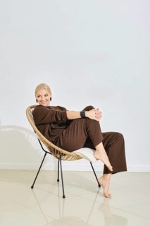 A barefoot woman dressed in brown lounge wear relaxes in a stylish chair, smiling and exuding a