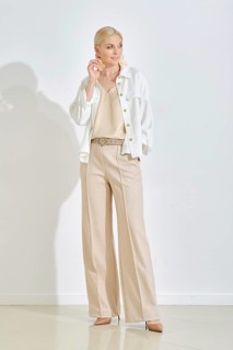 A woman dressed in a cream top and stylish beige trousers strikes a confident pose in a minimalist