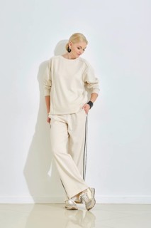 A woman dressed in a cozy beige outfit leans casually against a white wall, showcasing a relaxed