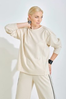 A woman showcases a light-toned casual outfit featuring a relaxed sweatshirt and stylish pants. She