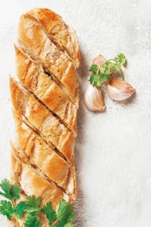 Garlic bread, baguette with garlic butter and herbs, on a light table, top view