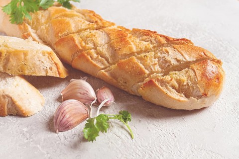 Garlic bread, baguette with garlic butter and herbs, on a light table, top view