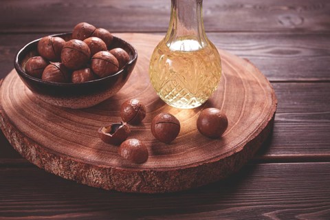 Bottle of macadamia oil, on a wooden board, with macadamia nuts, wooden background, selective
