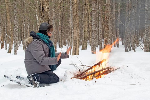 A woman warms herself by a campfire in winter, Gaspesie national park, Province of Quebec, Canada,