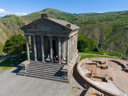 Ancient temple complex with columns and ruins against a green mountain background, aerial view,