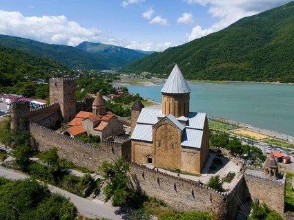 Historic fortress above a reservoir, surrounded by green hills in an idyllic setting, aerial view,