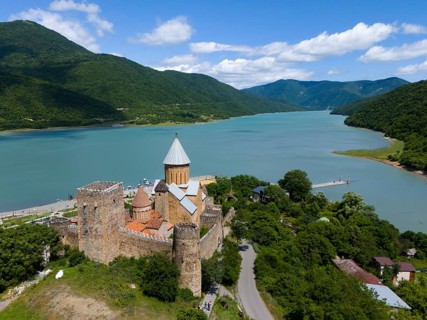 Medieval castle on the river surrounded by green mountains under a cloudy sky, aerial view, Ananuri