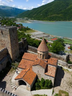 Red tiled roof of a medieval fortress church with castle walls and green lake panorama, aerial