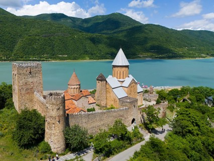 Medieval castle on the lake in front of forested mountains with peaceful atmosphere under blue sky,