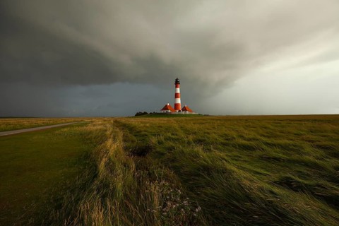 Illuminated Westerheversand lighthouse on the North Sea under dark storm clouds