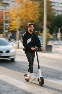 Ein junger Mann nimmt mit einem E-Scooter am öffentlichen Straßenverkehr in einer Stadt teil,