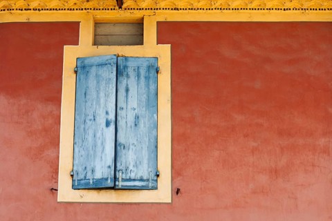 Red house façade with a window and closed blue shutters, Vaison la Romaine, Provence, France