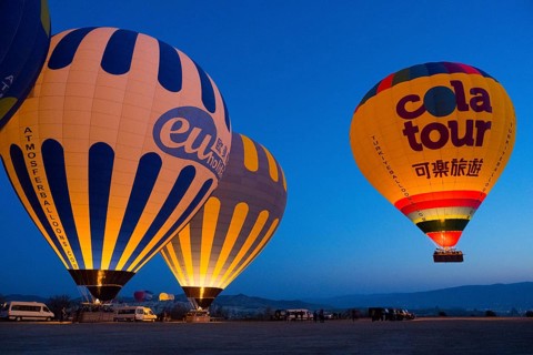 Glowing hot air balloons against a deep blue morning sky create a peaceful atmosphere on a plateau,