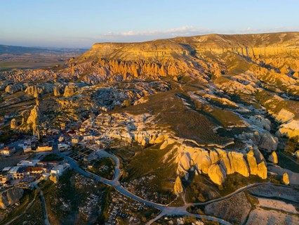 A picturesque landscape with rock formations and a small village in warm sunset light, aerial view,