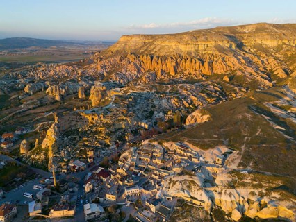 Stone formation at sunset over a village with a golden skyscape, aerial view, Göreme National Park,