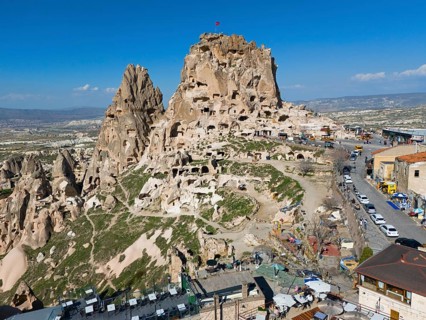 Historical rock formation with caves and buildings under a clear blue sky in a vast landscape,