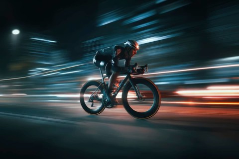 A cyclist, racing cyclist riding his racing bike fast on a road through a rural area in the dark,