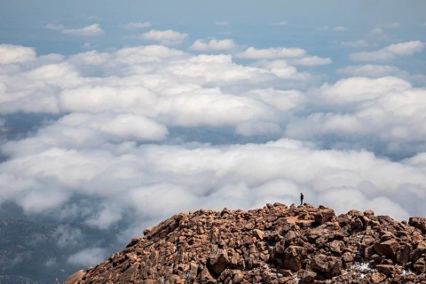 Colorado Springs, Colorado - A man stands on the rocks just below the summit of Pikes Peak, a 14,