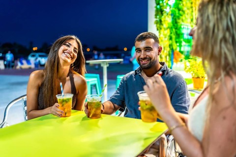 Three friends are laughing and chatting while enjoying refreshing beverages at a vibrant outdoor