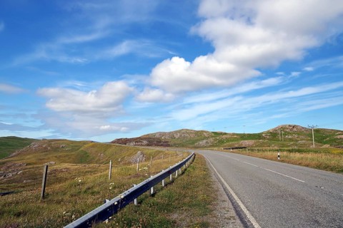 Empty road winds through hilly landscape under blue sky with clouds, Eshaness, Shetland Islands,