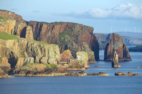 Coastal landscape with high cliffs lined with rocks and wind turbines in the background, Hillswick,
